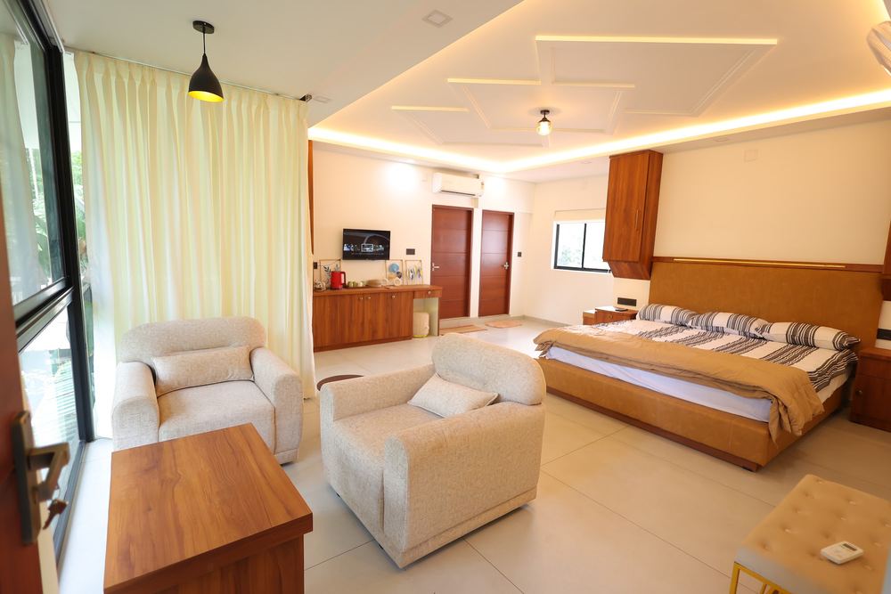 Armchairs and bed in one room, balcony doors open to green