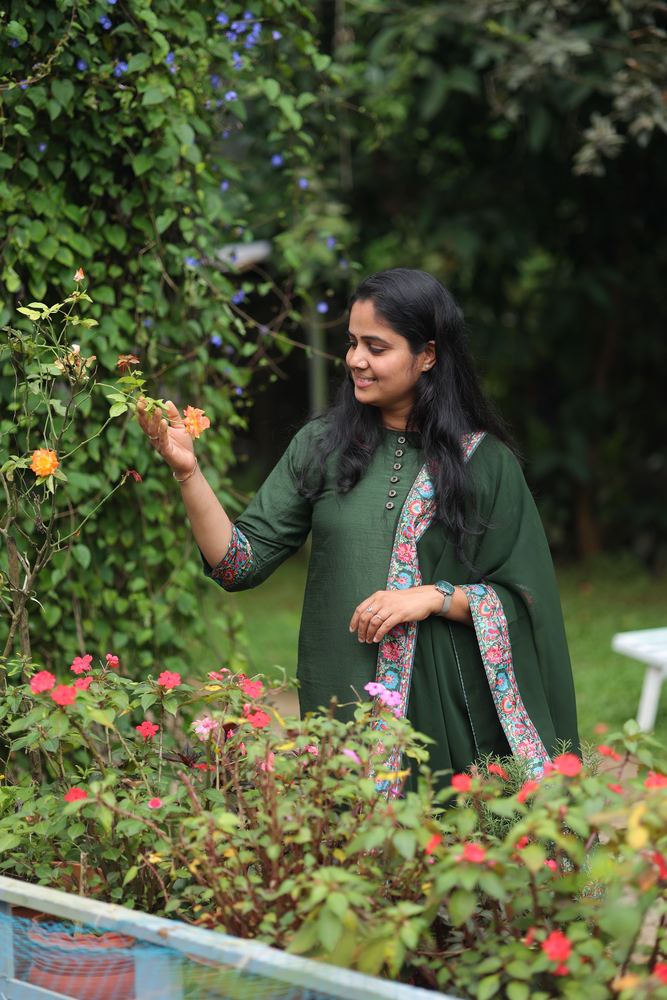 A woman looking at an orange rose in the garden