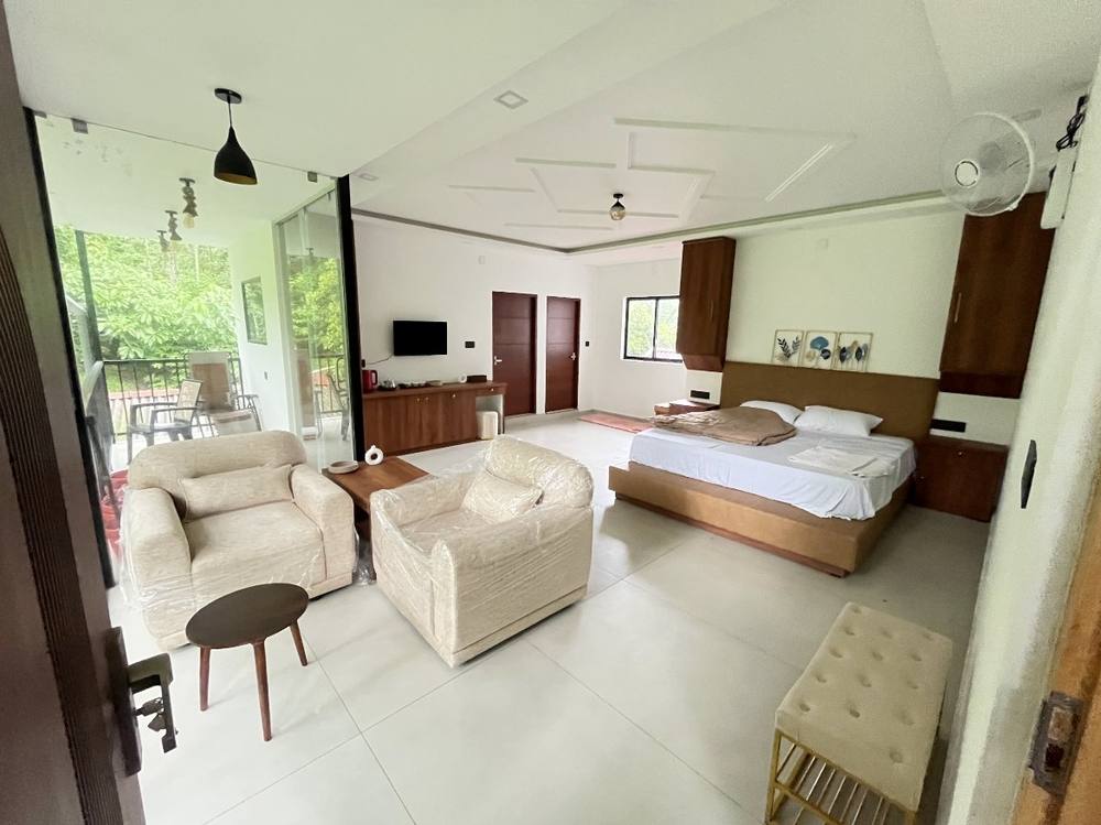 Room with king bed, sitting area and glass wall opening onto the balcony and coffee
