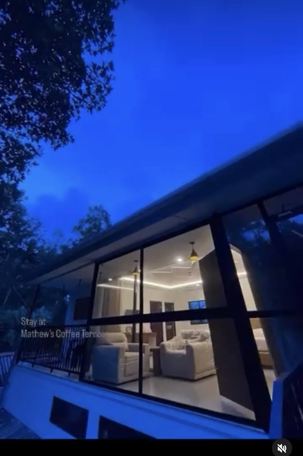 The glass rooms lit from inside at dusk, with the plantation dark around them